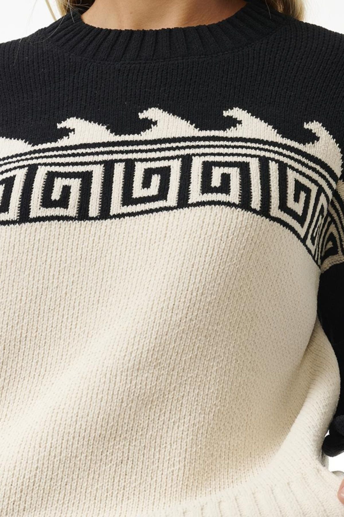 A close-up of the Rip Curl Soleil Knit Crew, an oversized sweater in recycled poly chenille with a black top, white bottom, and black-and-white geometric wave pattern; the wearer's head is not shown.