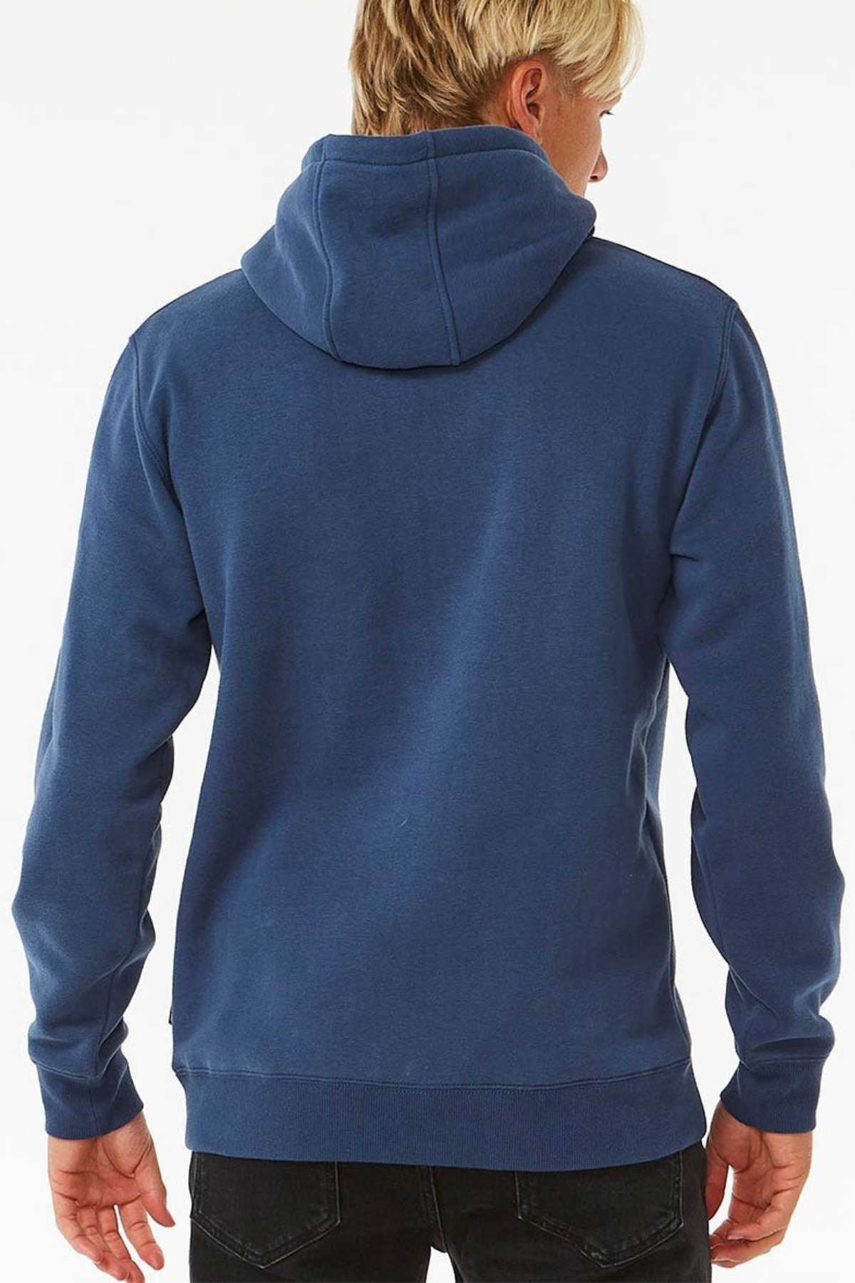 A blond-haired person facing away from the camera wears a blue Rip Curl Stapler Hood and black pants. The image highlights the hoodie’s back, hood, and long sleeves against a white backdrop.