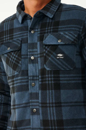 A person wore a blue and black plaid button-up shirt with two chest pockets, reminiscent of Rip Curl's Tofino Polar Fleece Jacket.