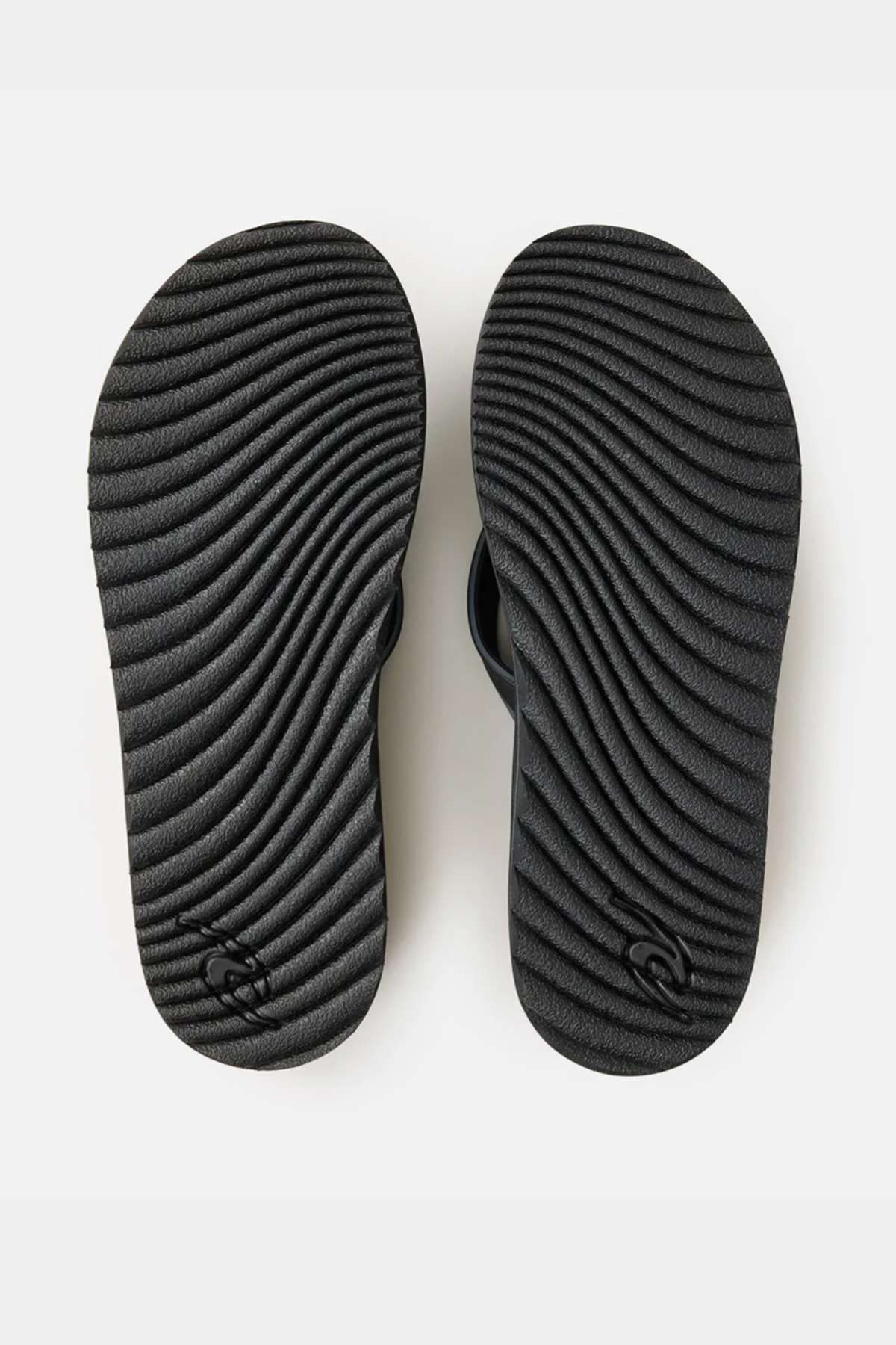 The Rip Curl Tunnels Bloom Thongs are black flip flops with textured, wavy grooves on the soles and a small logo near each heel, crafted from eco-friendly BLOOM algae foam, shown from the bottom against a white background.