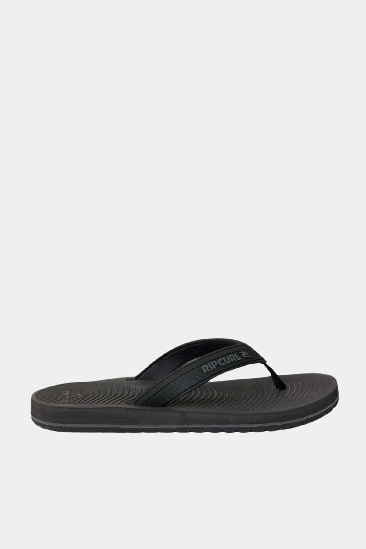 The Rip Curl Tunnels Bloom Thongs are black flip flops with a textured sole made from eco-friendly BLOOM algae foam and a simple strap featuring the "Rip Curl" logo, shown on a plain white background.