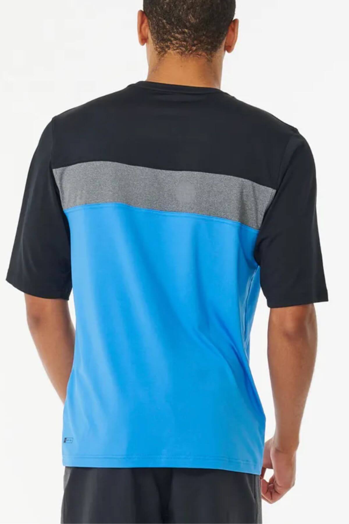 A man is seen from behind wearing the Rip Curl Undertow Short Sleeve UV Tee, which has a black top, gray stripe, and bright blue lower section. The UPF50+ tee provides extra sun protection, paired with black shorts.