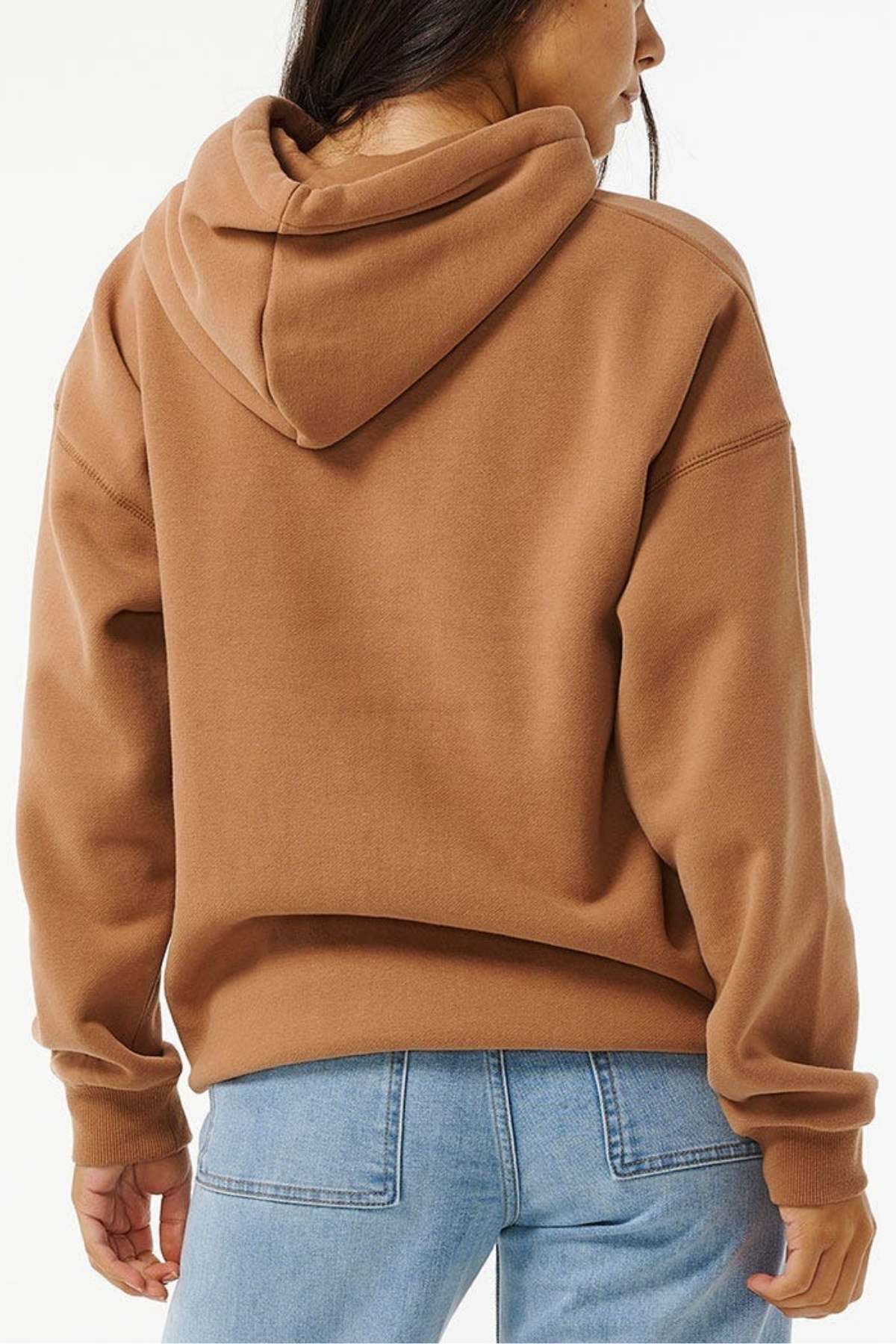 A person in an oversized Rip Curl Varsity Hoodie, with soft fleece lining and long sleeves, paired with light blue jeans stands against a plain white background, facing away from the camera.
