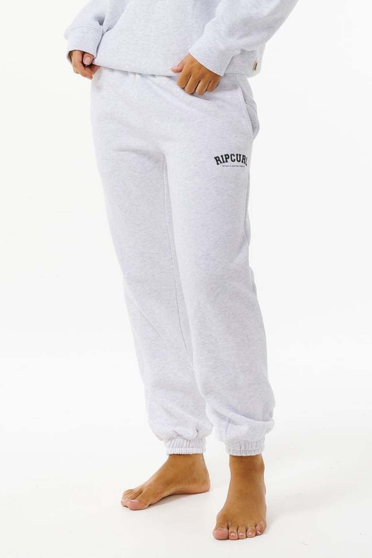 A person is shown barefoot, wearing Rip Curl Varsity Pants in light grey, made from soft Cotton Poly Fleece. Only the lower half is visible against a white background—ideal for casual, effortless style.