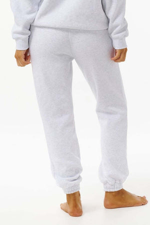 A person stands barefoot, seen from the back, wearing Rip Curl Varsity Pants in light gray with a matching soft Cotton Poly Fleece sweatshirt, set against a plain white background.