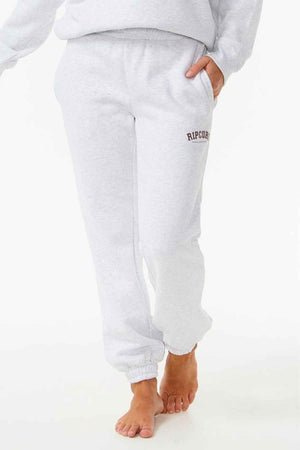 A person is wearing light gray Rip Curl Varsity Pants with "Ripcurl" on the upper left, made from Cotton Poly Fleece, featuring elastic cuffs. They are barefoot against a white background.