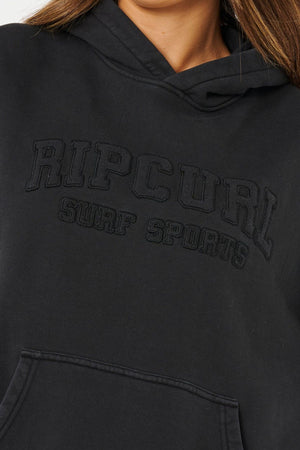 Close-up photo of someone in the Rip Curl Varsity Sports Oversized Hood, made from 100% cotton with "RIP CURL SURF SPORTS" embroidered in black. Only their lower face and hair are shown.