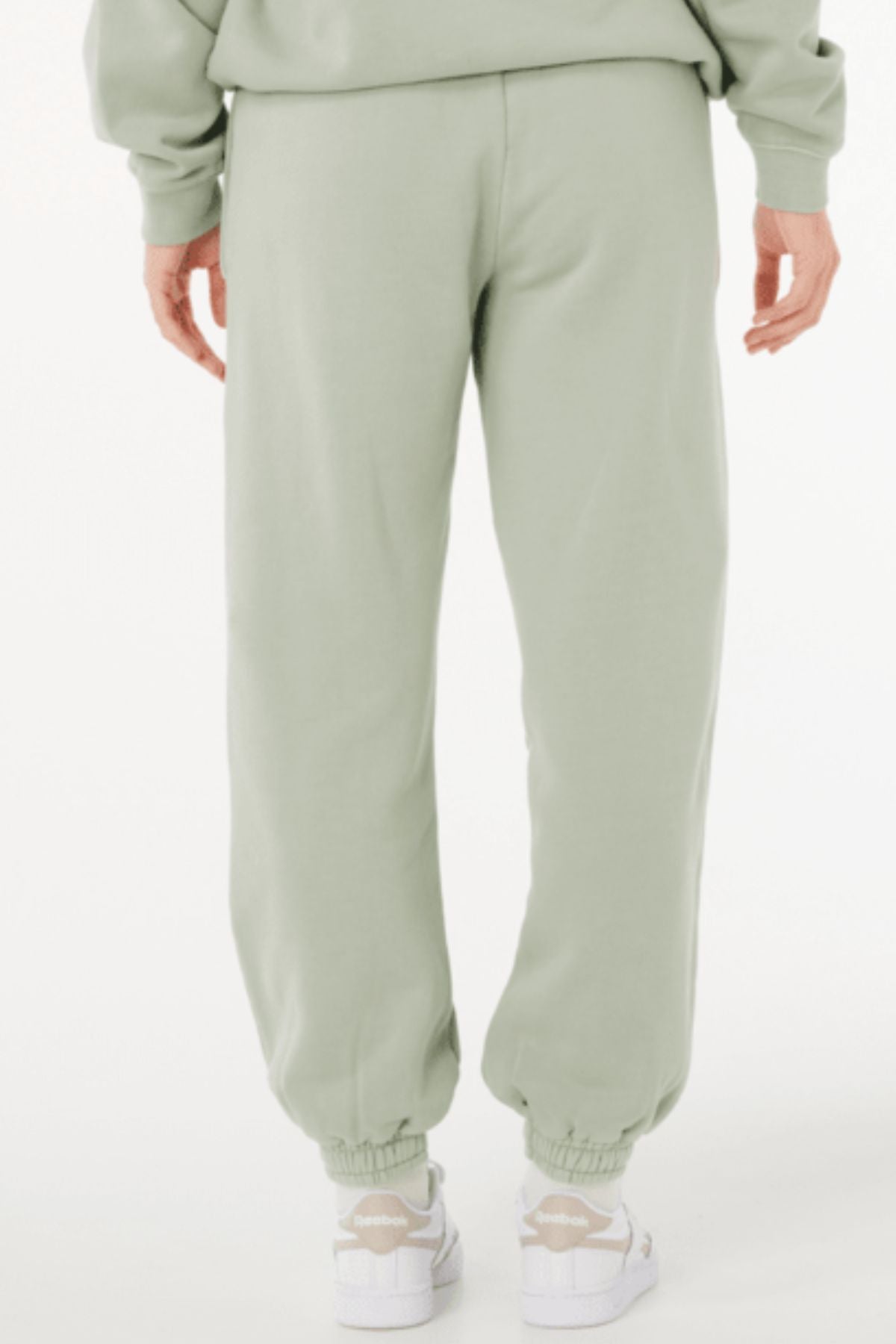A person shown from the back wears Rip Curl Varsity Sports Track Pant in light green with white sneakers against a plain white background.