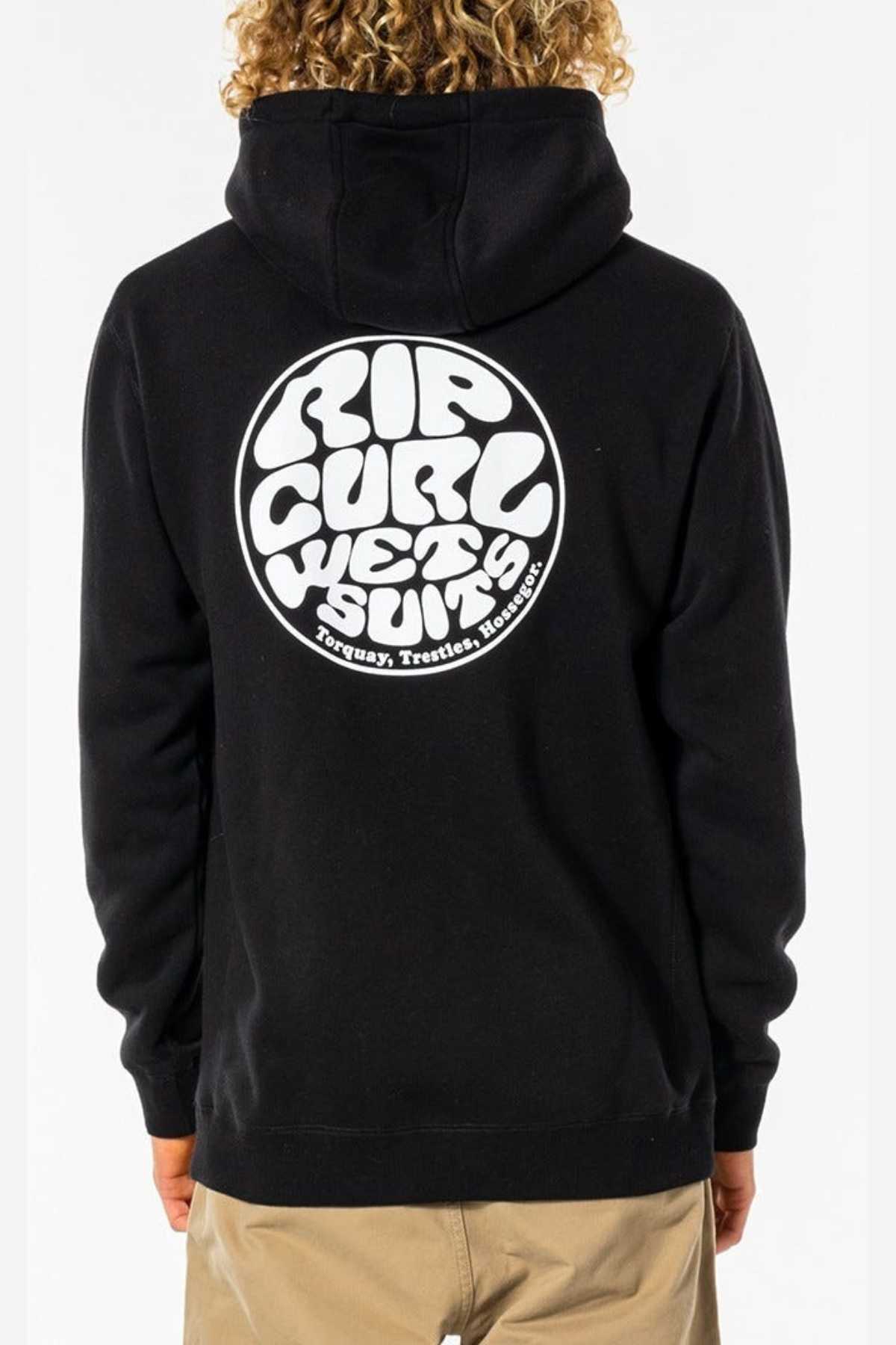 Wearing a black Rip Curl Wetsuit Icon Hood made from organic cotton poly fleece, featuring a bold circular logo and “Torquay, Trestles, Hossegor” on the back, plus a kanga pocket for comfort. Their back faces the camera.
