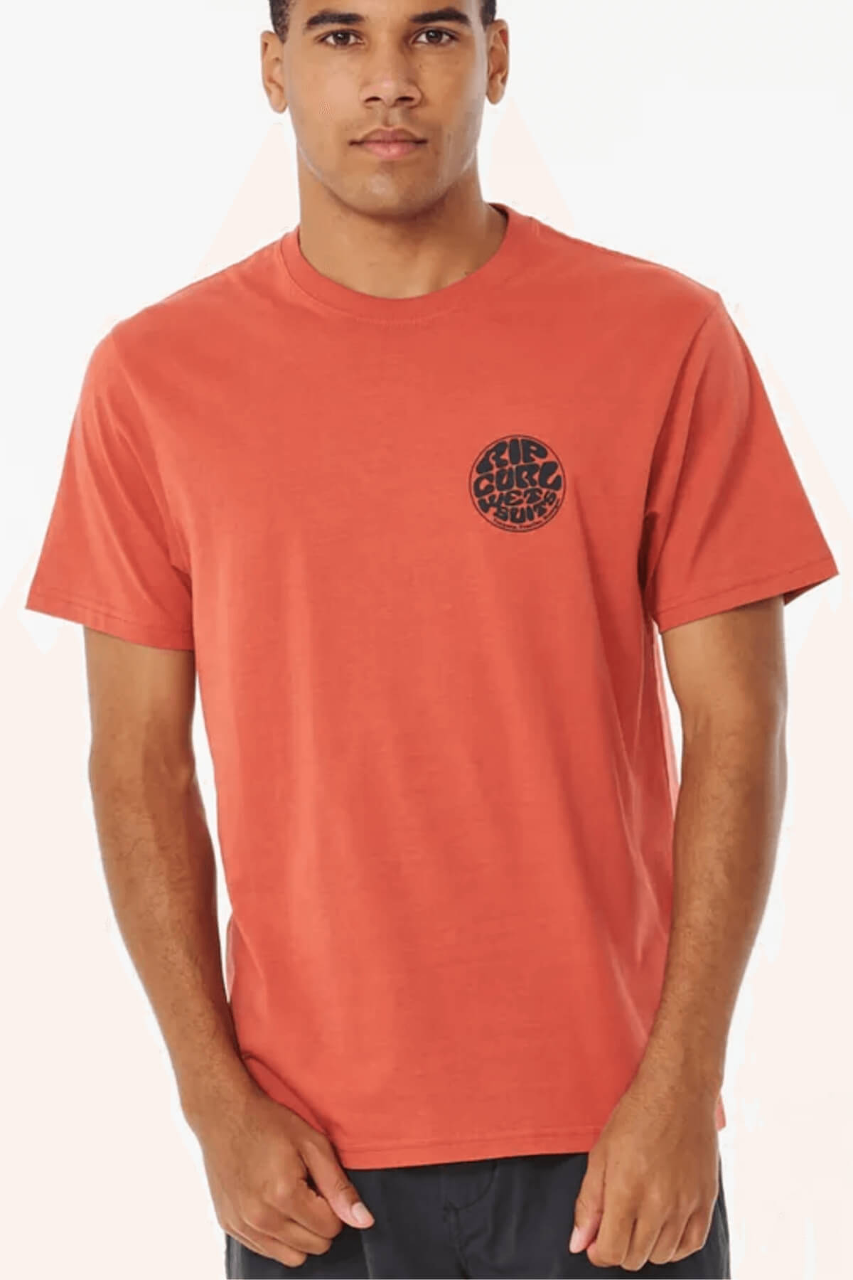 A man wears the Rip Curl Wetsuit Icon Tee—short-sleeved, burnt orange, breathable cotton with a small round black logo on the left chest—standing against a light background.