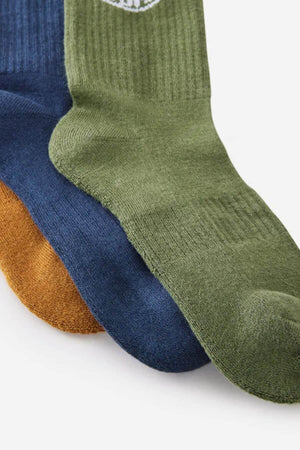 Three Rip Curl Wetty Crew socks in green, blue, and mustard yellow with a ribbed texture and arch support overlap on a light background.