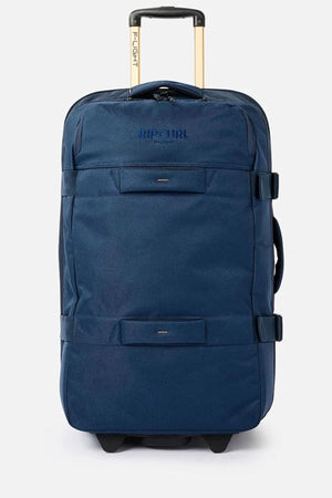 The Rip Curl F-Light Global 100L Sapphire Travel Bag, crafted from recycled polyester, is a spacious and stylish option in blue. It features adjustable compression straps, the "Rip Curl" logo prominently displayed, and a telescopic handle marked "Flight." The suitcase is perfectly captured standing upright against a plain white background.