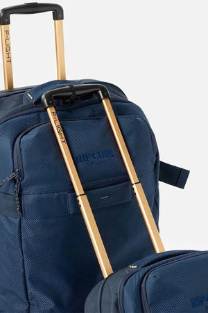 Two Rip Curl F-Light Global 100L Sapphire travel bags with gold handles stand upright. The brand name is visible on the larger suitcase. Crafted from recycled polyester, their extended handles and compression straps showcase mobility and functionality.