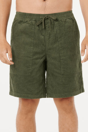 A person wearing Rip Curl Classic Surf Cord Volley shorts in olive green cotton corduroy with elastic waistband, drawstring, and side pockets. The cropped photo highlights the vintage surf shorts vibe and part of the torso and legs.