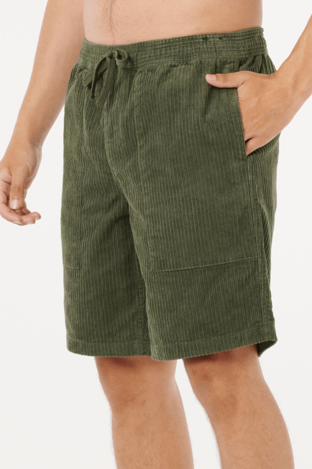 A person wearing Rip Curl Classic Surf Cord Volley shorts—olive green, knee-length cotton corduroy with elastic waistband and drawstring, hand in pocket. A classic style inspired by vintage surf shorts.