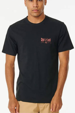 A man stands against a white background wearing the Rip Curl Affinity Tee, a black 100% cotton short-sleeve shirt with a small red "Rip Curl" logo on the left chest, paired with tan shorts.