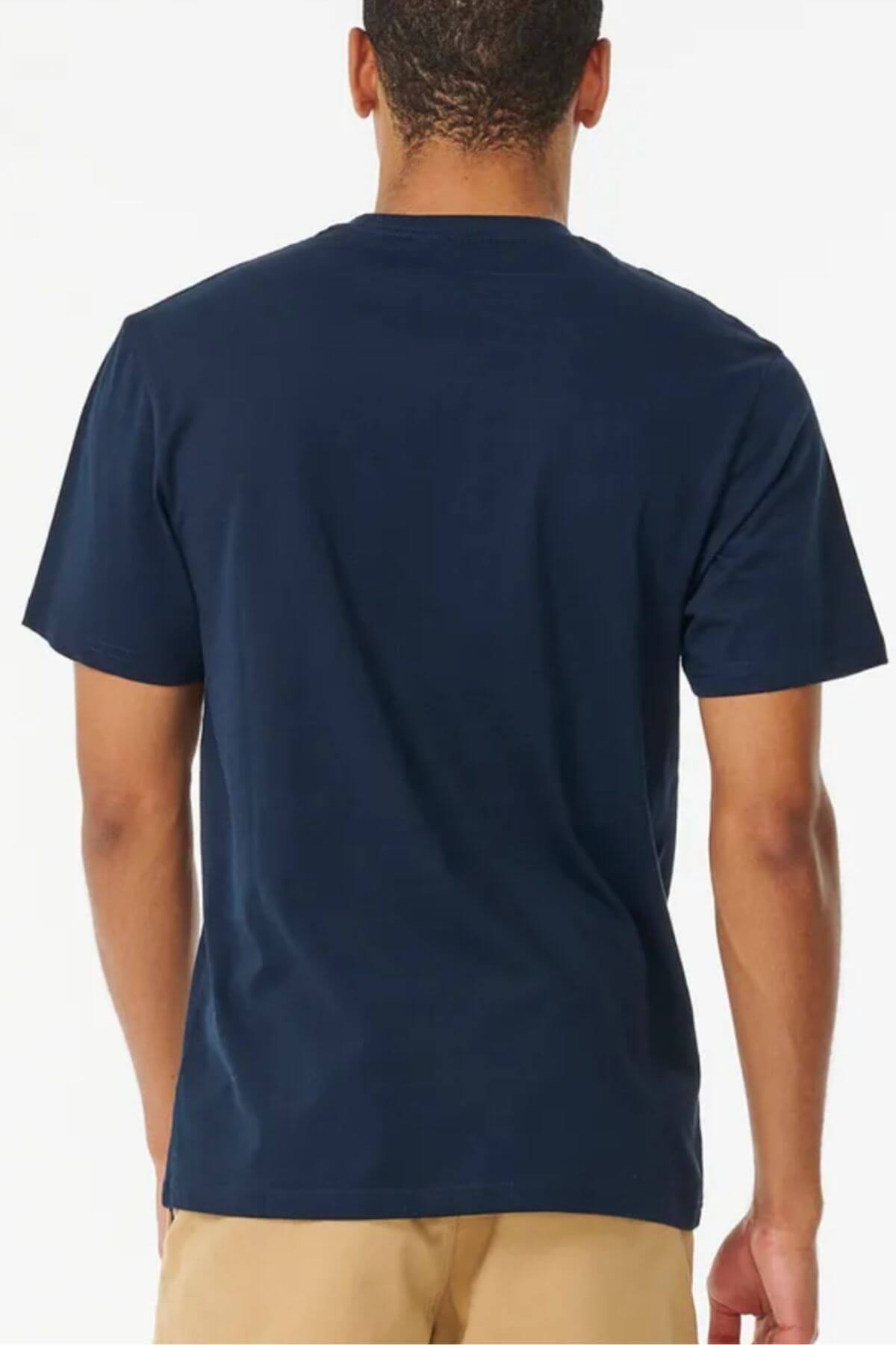 A person wearing a navy Rip Curl Brand Icon Tee with beige pants stands against a light backdrop, showcasing the 100% cotton T-shirt's standard fit and relaxed style.