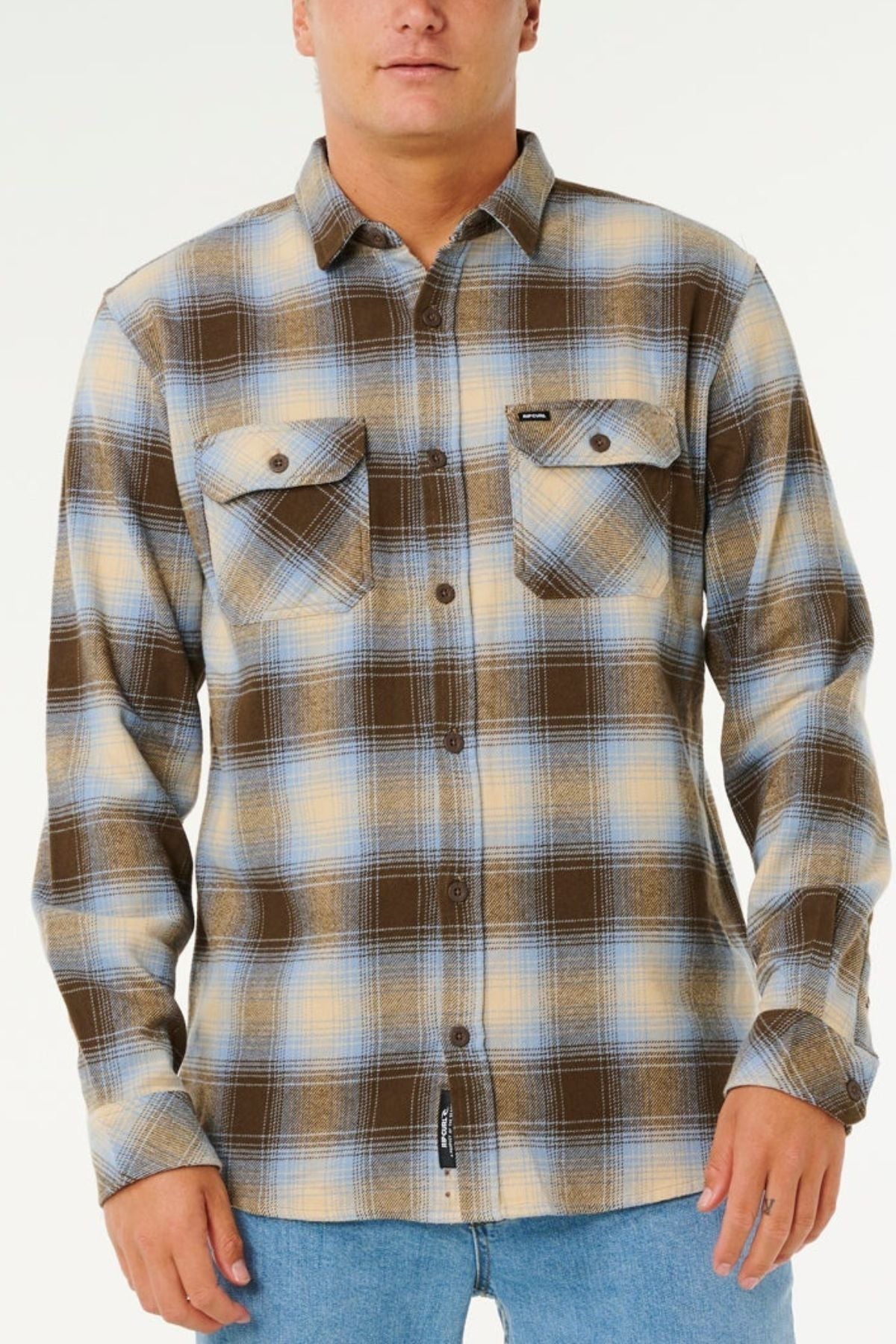 A person wears the Rip Curl Count Flannel Shirt—long-sleeve, button-up, in brown, blue, and beige heavy brushed fabric—with light blue jeans against a plain background for a sustainable fashion look.