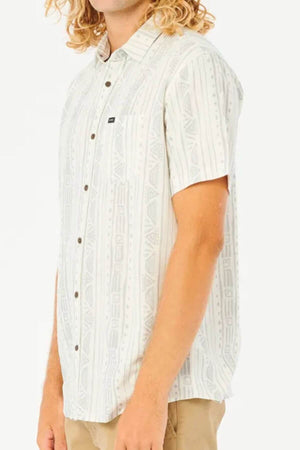 A person with long, curly blonde hair is shown from the side wearing a light-colored Rip Curl Nocturnal Short Sleeve Shirt with a subtle geometric pattern and tan pants.