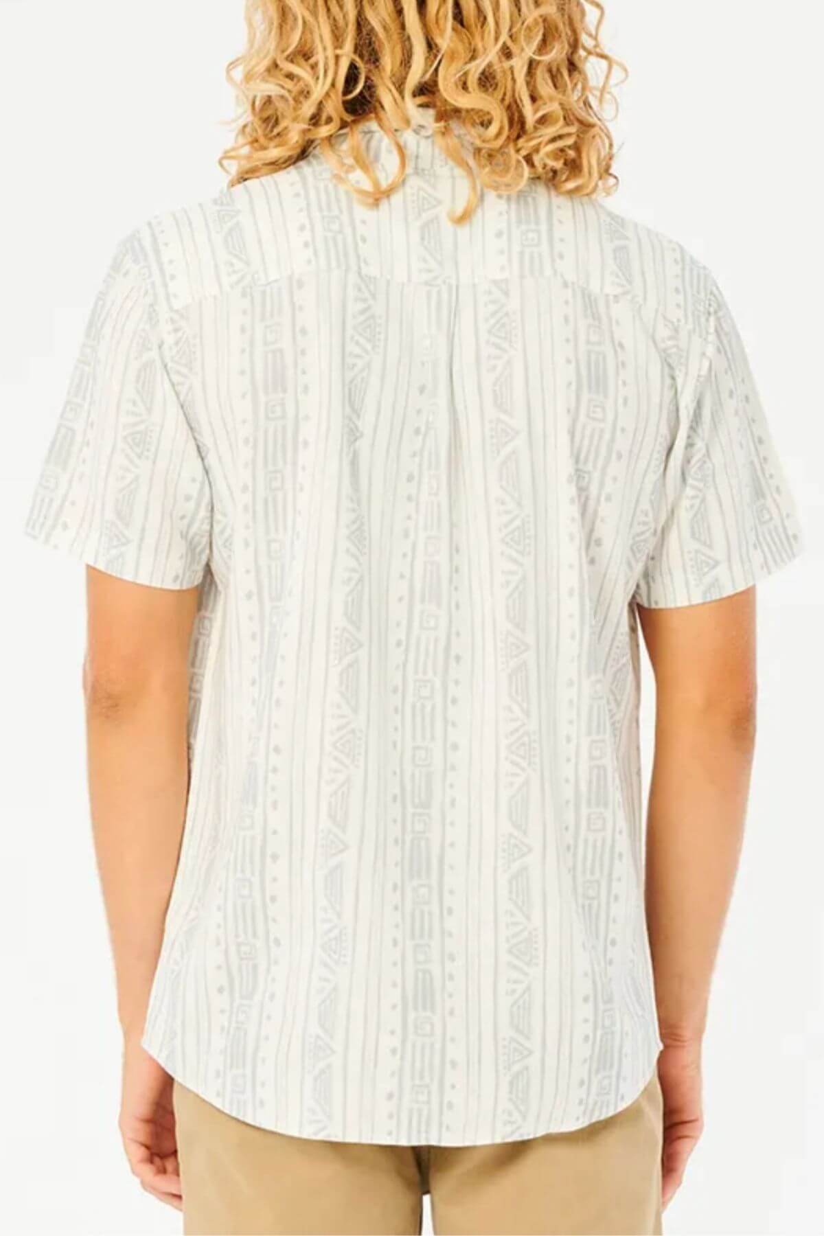 A person with long, curly blond hair is shown from the back wearing a light Rip Curl Nocturnal Short Sleeve Shirt with a subtle geometric pattern in a soft viscose linen blend and beige pants against a white background.