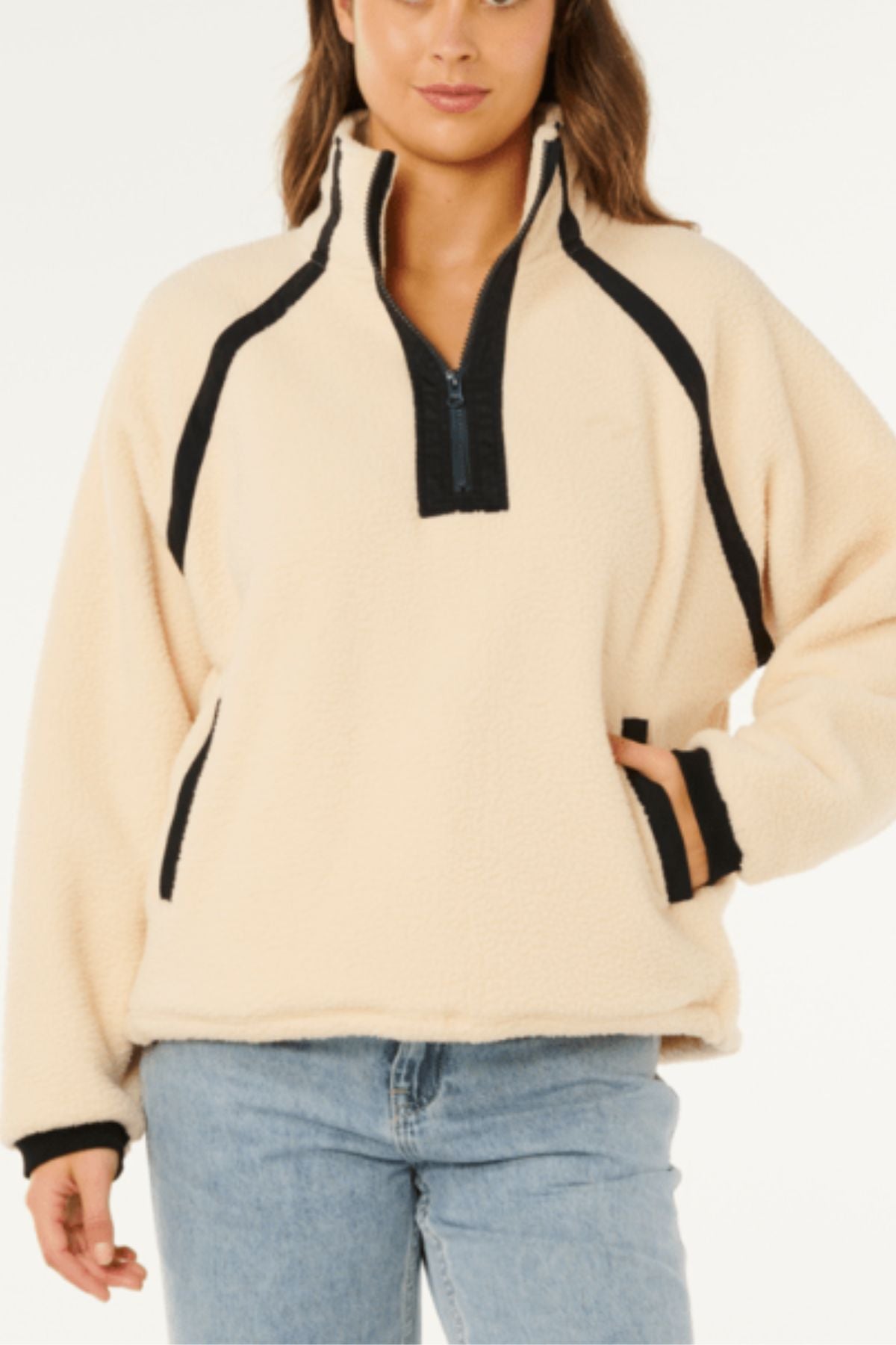 A person wearing the Rip Curl Surf Club Heritage Polar fleece pullover with black trim and a half-zip front, paired with blue jeans. One hand is in a pocket, and the photo is cropped just above the knees.