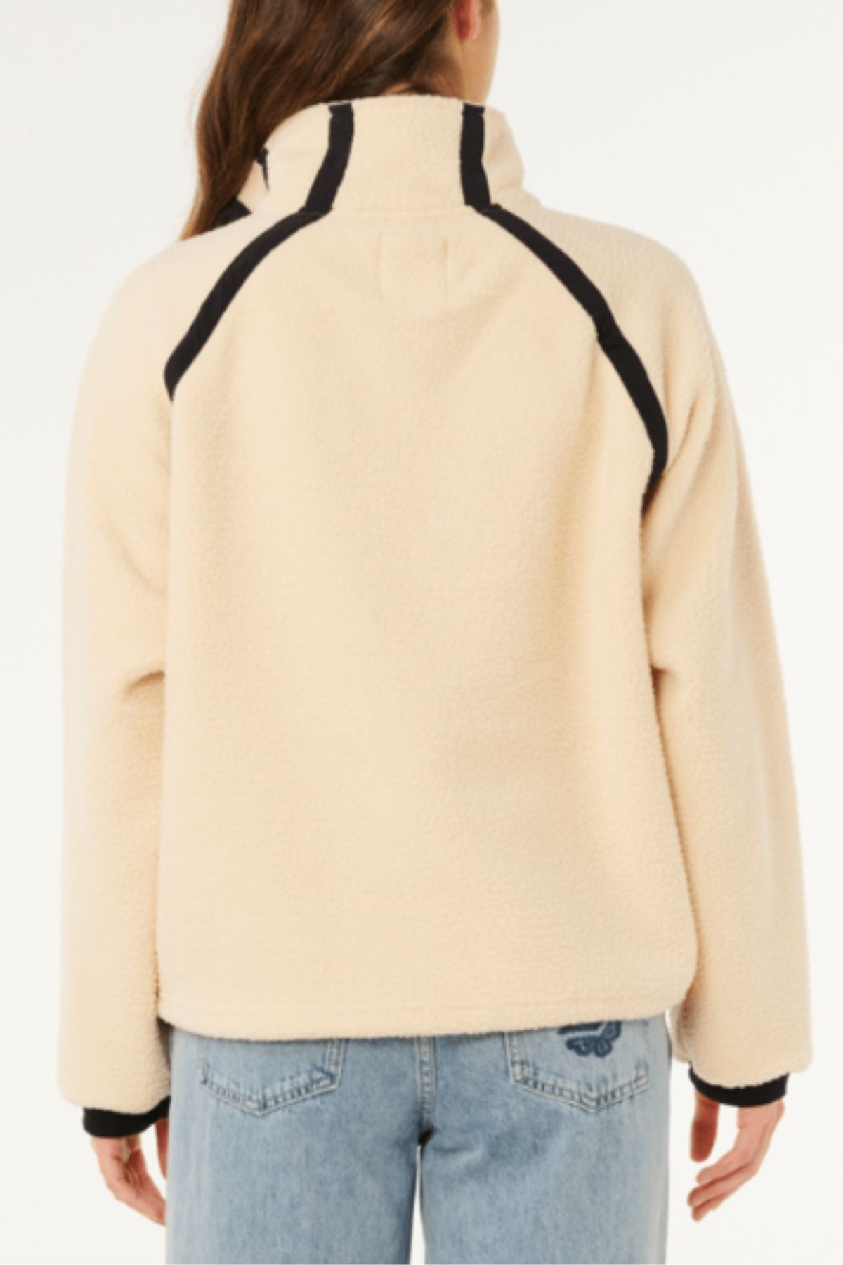 A person is seen from the back wearing the Rip Curl Surf Club Heritage Polar fleece jacket in light beige with black trim, paired with light blue jeans, set against a plain white background.