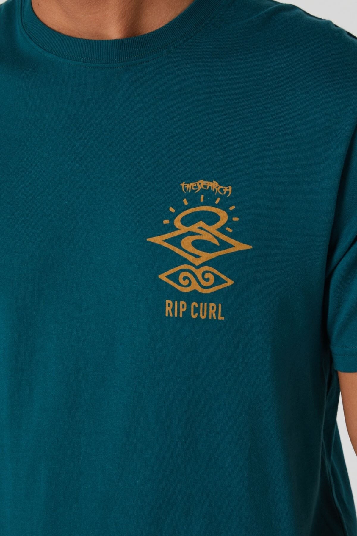 Someone wearing the Rip Curl Search Icon Tee in teal, featuring a yellow geometric graphic and "RIP CURL" text on the chest.