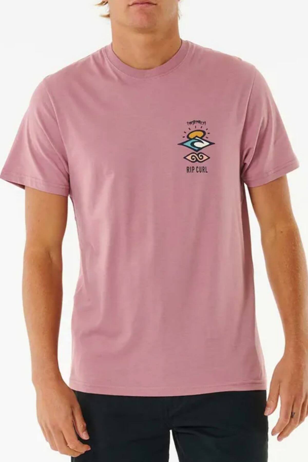 A person is wearing the Rip Curl Search Icon Tee, a pink cotton shirt with a small logo and text on the chest, paired with black pants against a plain white background.