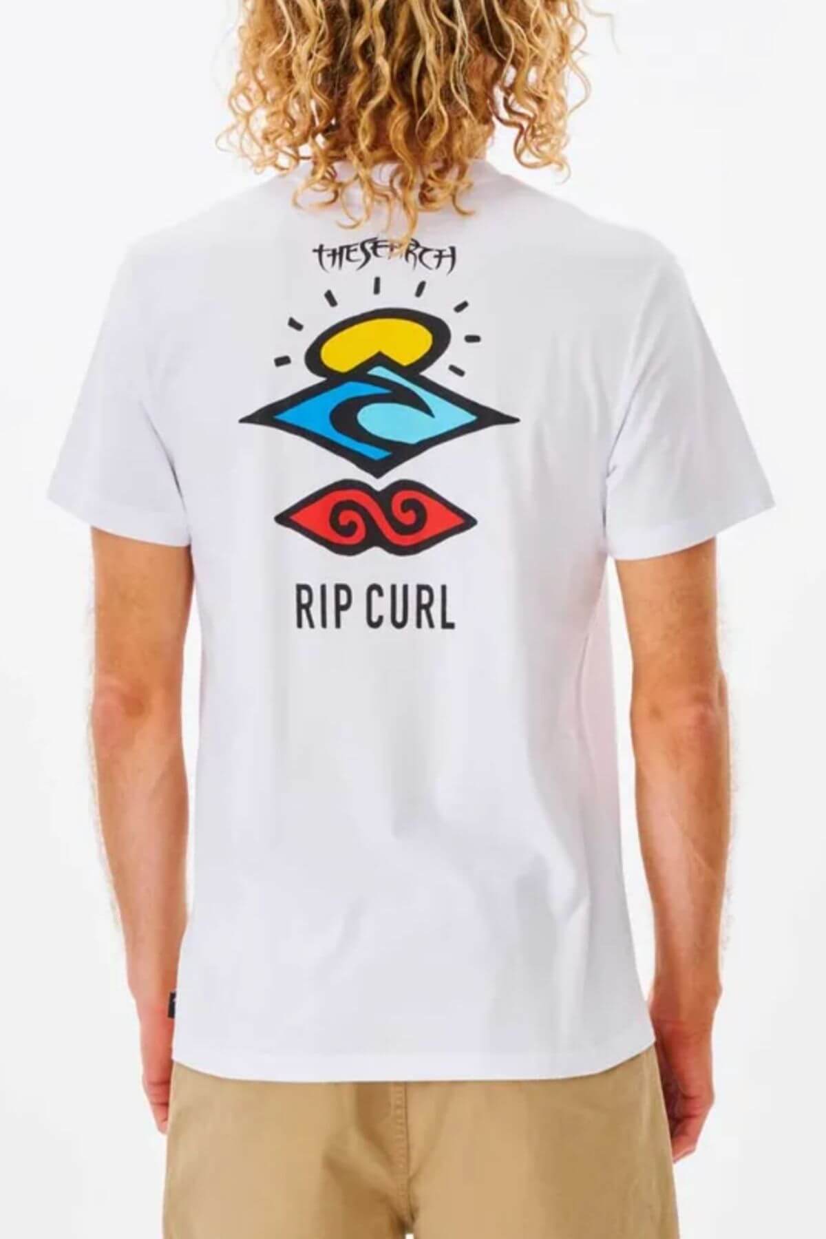 Person with curly blonde hair wearing the Rip Curl Search Icon Tee—a white 100% cotton T-shirt with colorful abstract graphics and "The Search" on the back.