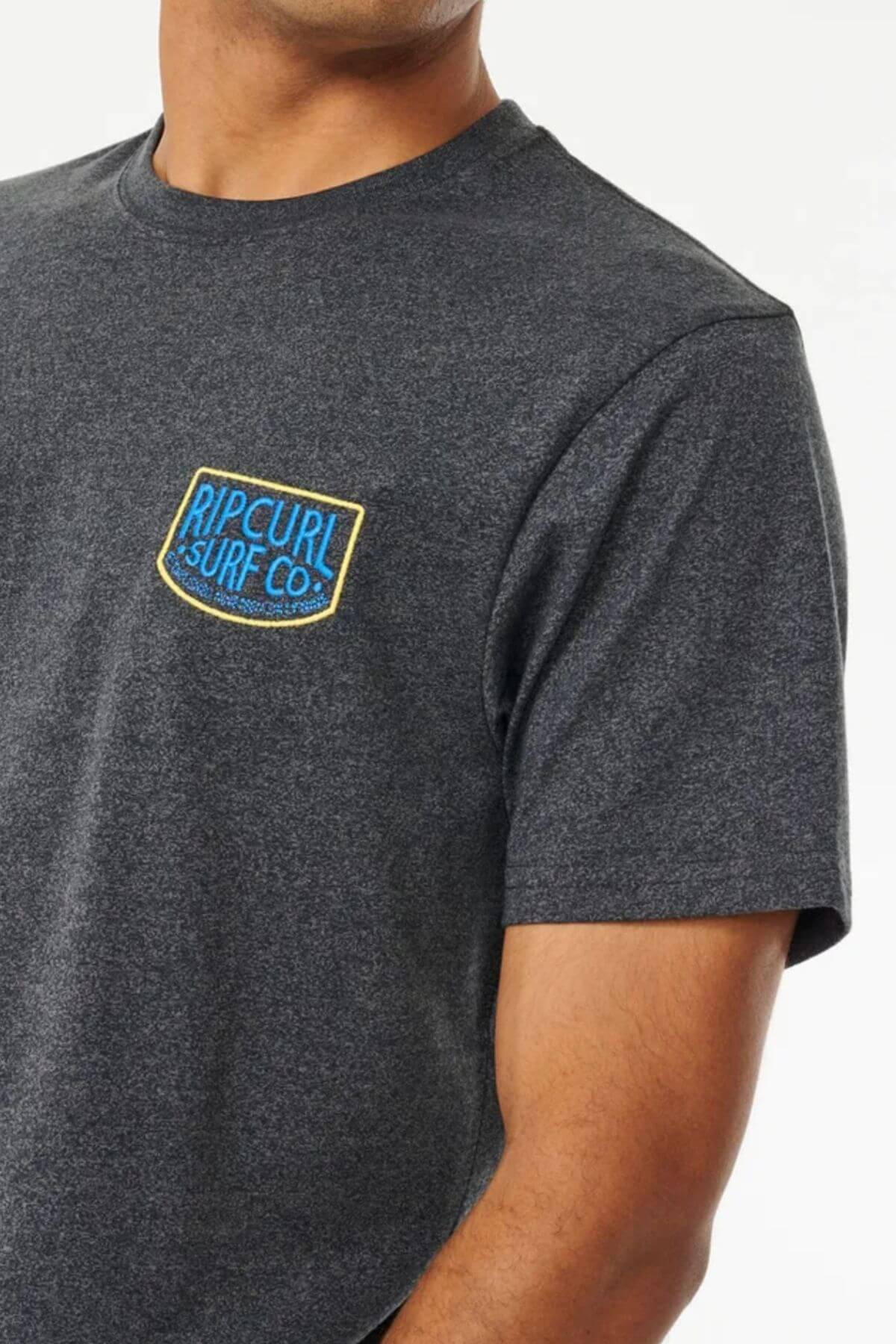 A person wears a dark gray Rip Curl Too Easy Embroid Tee, crafted from 100% cotton, featuring the "Rip Curl" patch elegantly embroidered on the chest against a white background.
