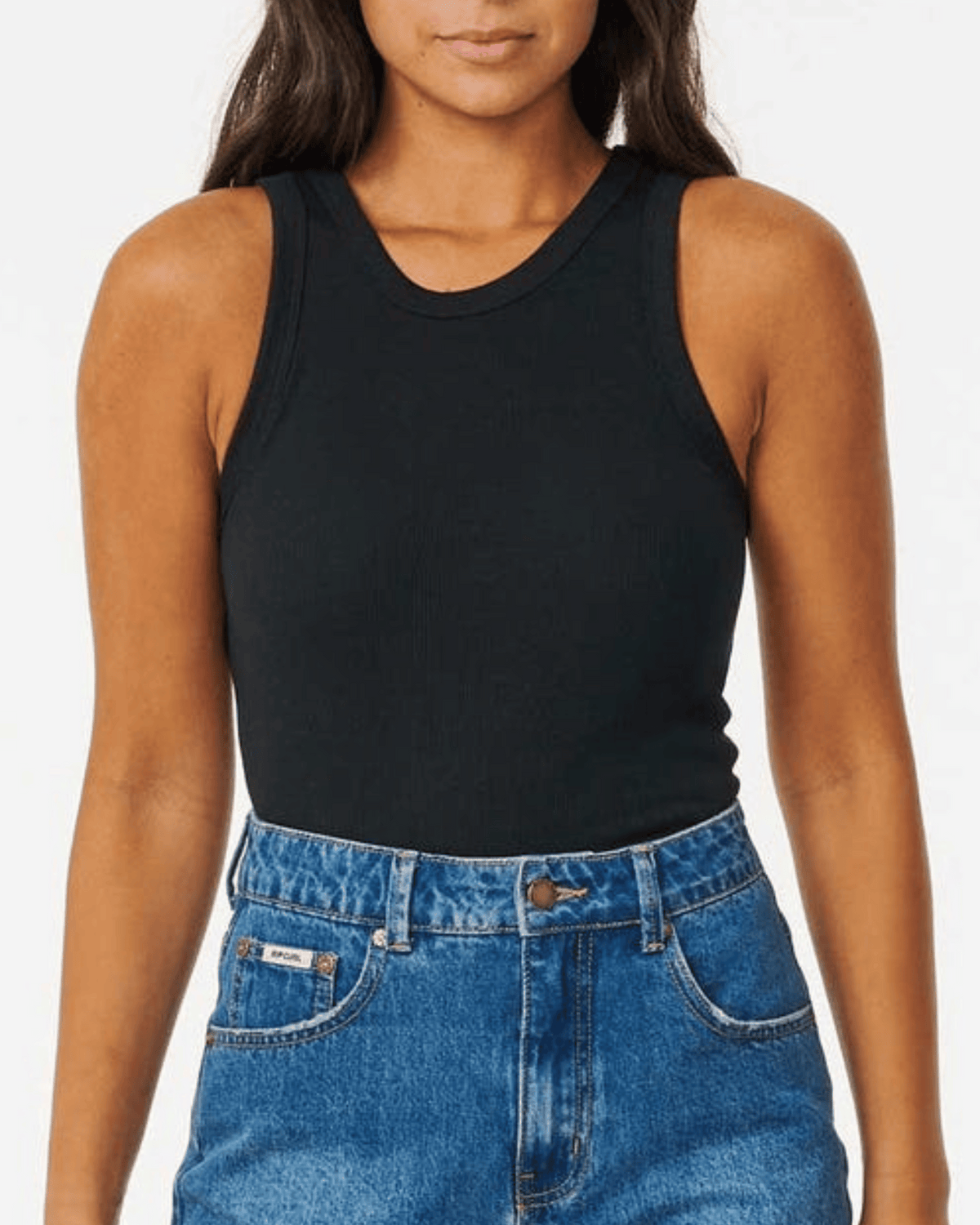 A person wears a black Rip Curl Classic Ribbed Tank and high-waisted blue jeans, standing against a plain white background. The image is cropped from the shoulders to the hips.