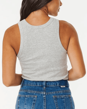 A person with long hair, facing away from the camera, wears the Rip Curl Classic Ribbed Tank in gray paired with blue jeans. The cotton elastane blend offers comfort and style against a plain white backdrop.