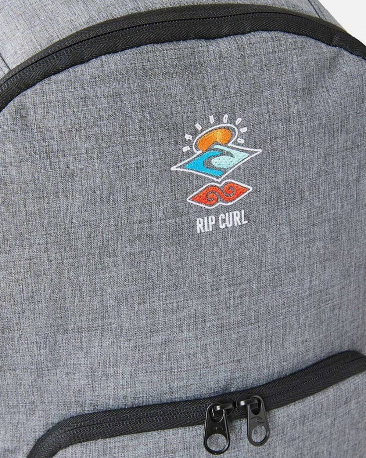 Close-up of the Rip Curl Evo 24L Icons Of Surf Backpack in grey recycled polyester, featuring a colorful embroidered wave, sun, and water logo above a zippered pocket. Includes a convenient laptop section.