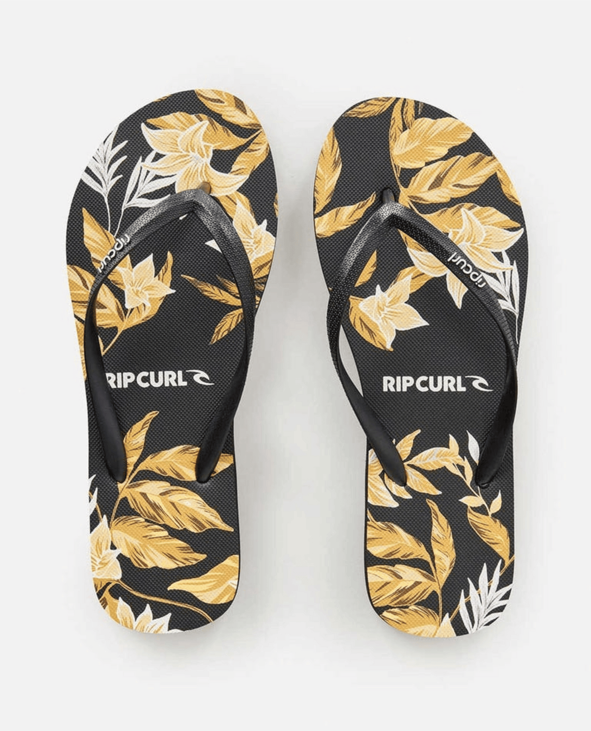 A pair of Rip Curl La Isla Bloom Thongs featuring black soles with a yellow and white floral pattern. The black straps are adorned with the discreetly printed Rip Curl logo. Crafted from BLOOM™ algae blended foam for a sustainable touch, the background remains plain white.
