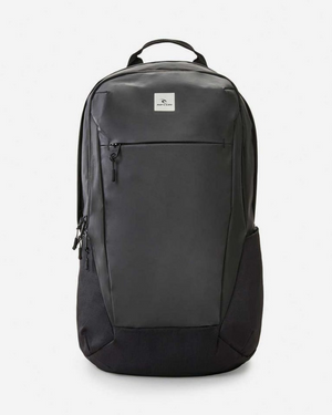 The Rip Curl Overtime 30L Backpack is a sleek black bag made from recycled polyester. It features a minimalist design with side mesh pockets, a front zipper pocket, and a top handle. A small logo patch decorates the upper front, enhanced by smooth, streamlined contours.