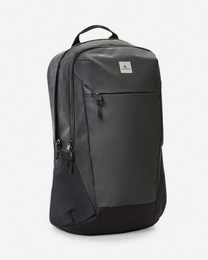 The Rip Curl Overtime 30L Backpack is a sleek black bag with a minimalist design, featuring a large front zip pocket, two side zippers, and a discreet logo. Made from recycled polyester, it has a top carrying handle and smooth texture, ideal for any adventure.