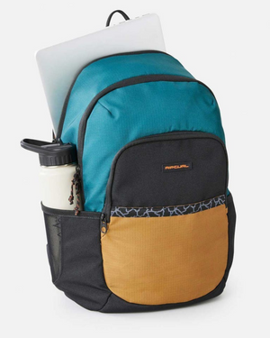 Meet the Rip Curl Ozone 30L Journeys Backpack: eco-friendly, crafted from recycled polyester in a stylish teal and black with a brown front pocket. It discreetly fits a laptop in the main compartment and snugly holds a white water bottle in the side pocket—perfect for travel.