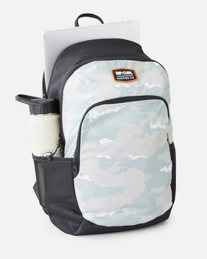 The Rip Curl Ozone 30L School Backpack in light camo, made from recycled polyester, features a front pocket, side mesh pocket with water bottle, and a laptop partly visible in the main compartment against a white background.