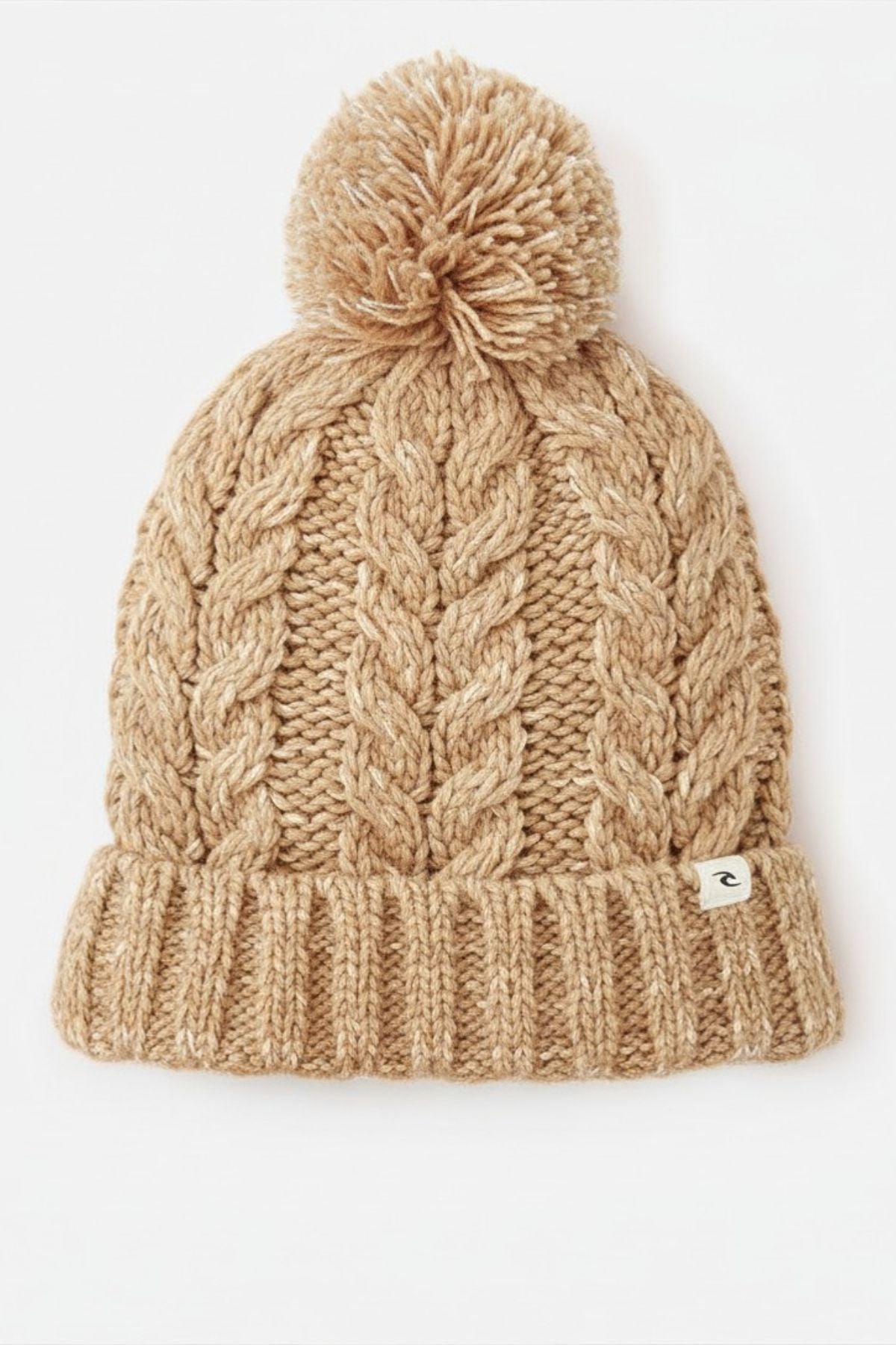 The Rip Curl Premium Reg Pom Pom Beanie is a beige cable knit hat with thick patterns, a folded brim, a small Rip Curl fabric tag, and a large removable pom-pom on top.