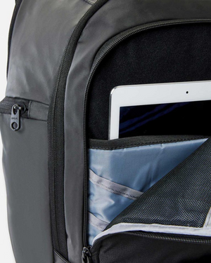A close-up of the Rip Curl Posse 33L Backpack features a partially unzipped front pocket with a tablet or slim laptop in a light gray sleeve. Crafted from water-resistant recycled polyester, it offers both durability and eco-friendly style.