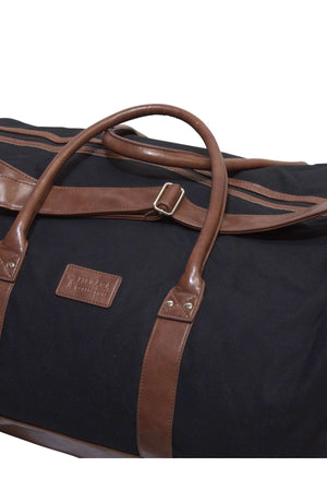 The Pilbara Long Weekender Bag by Ritemate is a black duffel crafted from the finest quality canvas and leather. It boasts brown leather handles, trim, and a name tag with text. A rectangular leather patch with embossed text enhances the front, while the main compartment features a zipper closure—making it perfect for weekend getaways.