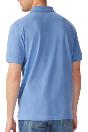 A man stands with his back to the camera in a light blue RM Williams Rod Polo and blue jeans, showcasing the rear view of the shirt.