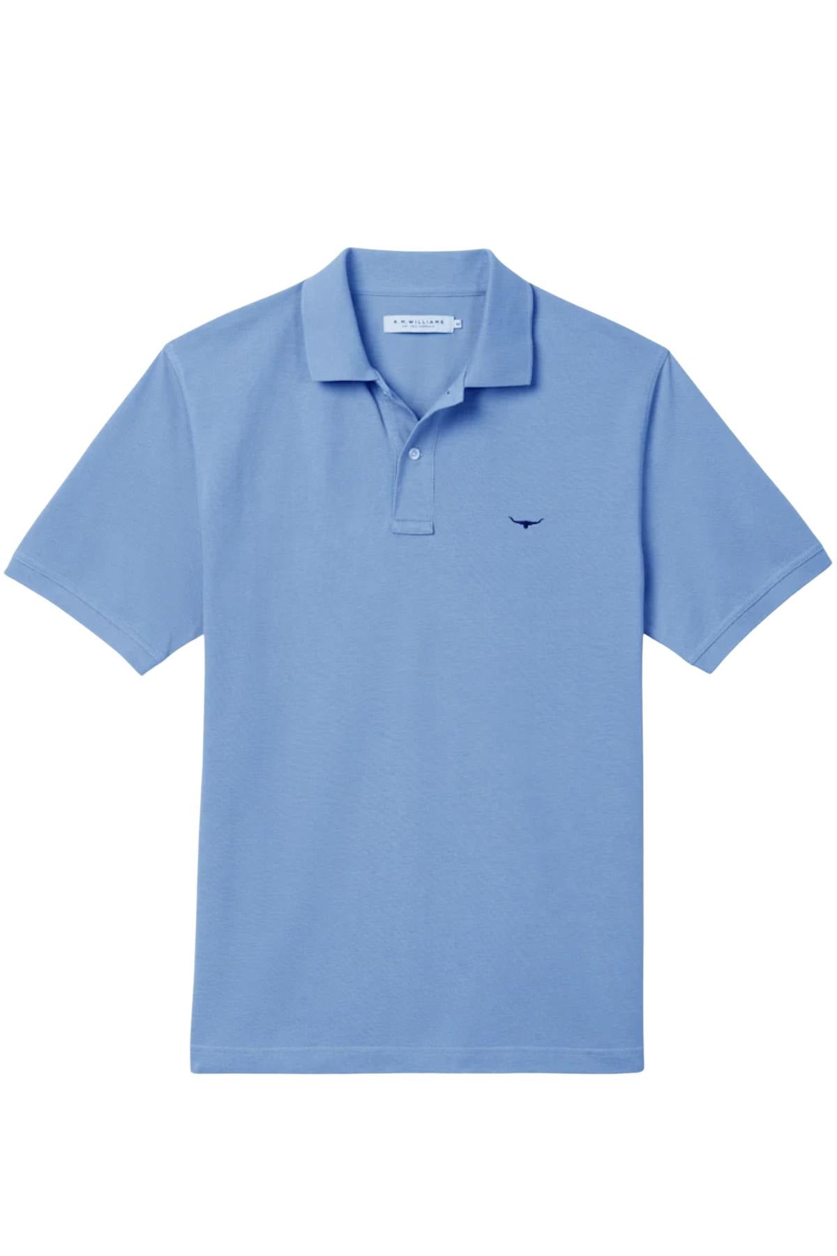 The RM Williams Rod Polo is a light blue classic polo shirt with a collar, button placket, and a small dark blue logo on the left chest. Made from soft organic cotton, it's shown on a plain white background.