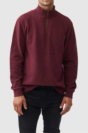 A man wears a maroon Rodd & Gunn Alton Ave Sweat with black pants, standing against a light gray background. His face is partially out of frame, and his hands are relaxed at his sides.