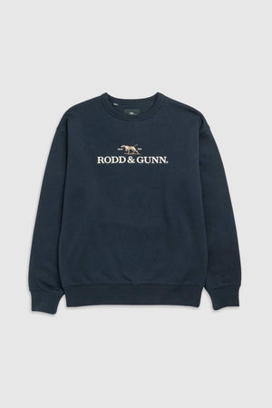 A navy blue Rodd & Gunn Gunn Logo Sweat features the text "RODD & GUNN" with a small embroidered dog logo above it. Made from premium USA Cotton, this crewneck includes ribbed cuffs and a ribbed hem, all set against a plain light gray background.