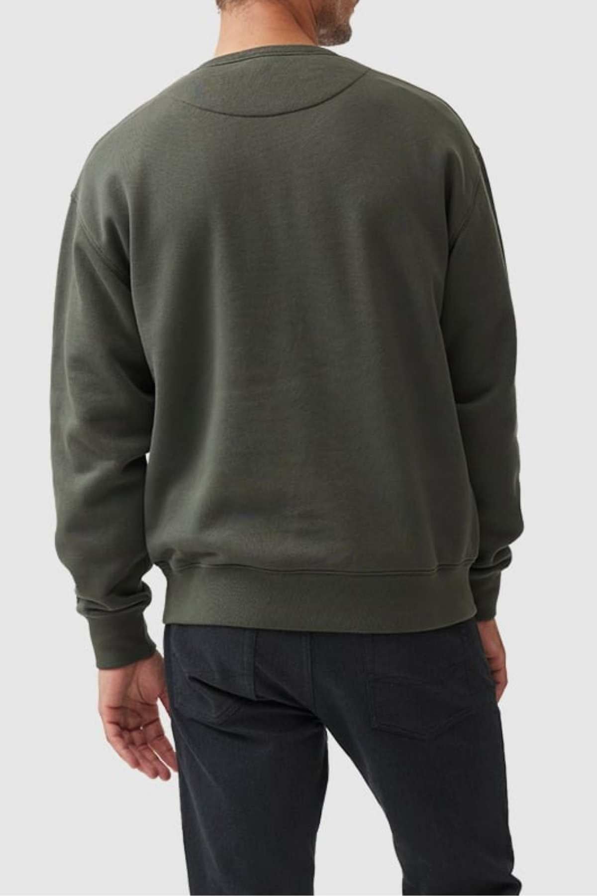 A person stands with their back to the camera, wearing a dark green Rodd & Gunn Gunn Logo Sweat and black pants. The background is a plain light color.