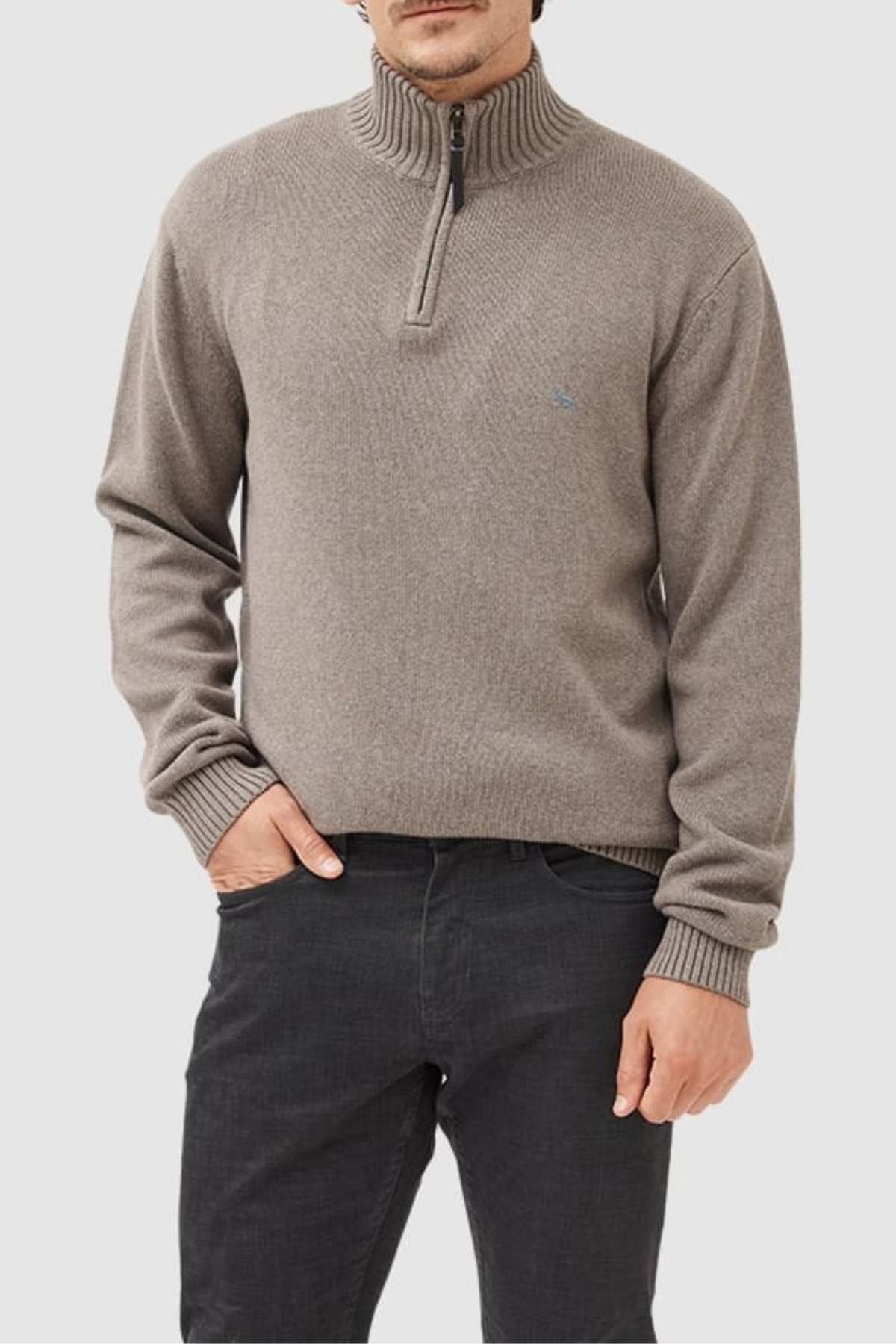 A man in the Rodd & Gunn Merrick Bay Knit, made from 100% cotton with a premium YKK zip, and dark jeans stands with one hand in his pocket against a plain light background.
