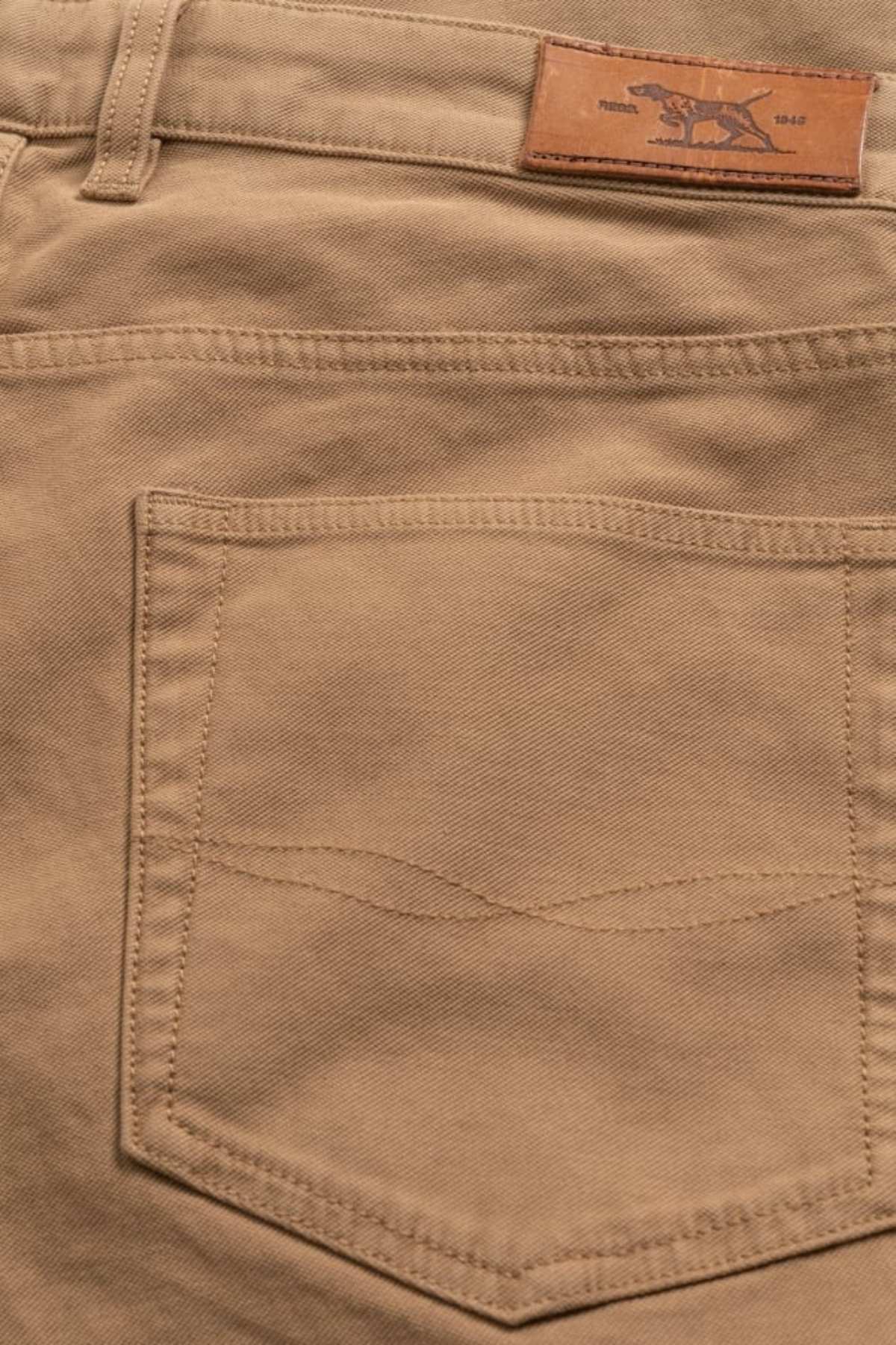 Close-up of the back pocket on Rodd & Gunn Motion 2 Straight Jean, showcasing a visible stitching pattern. Designed with comfort stretch motion fabric for ease, it features a waistband with belt loops and a small leather patch with an embossed logo near the top.