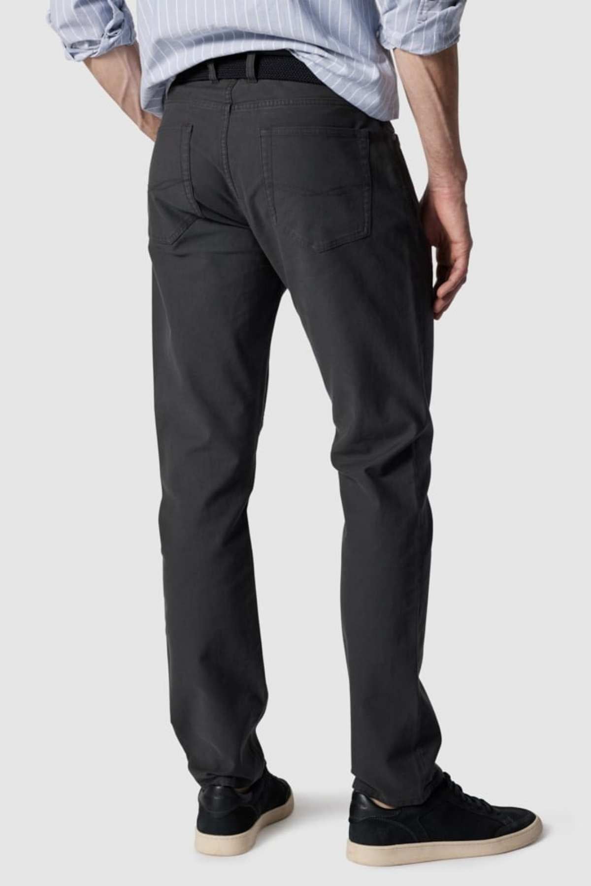 The individual is wearing a striped shirt with Rodd & Gunn Motion 2 Straight Jeans and a black belt. Their black sneakers feature white soles. Posed with their back to the camera against a plain backdrop, the outfit highlights comfort stretch fabric.