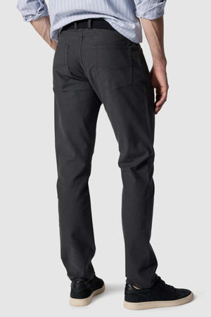 The individual is wearing a striped shirt with Rodd & Gunn Motion 2 Straight Jeans and a black belt. Their black sneakers feature white soles. Posed with their back to the camera against a plain backdrop, the outfit highlights comfort stretch fabric.